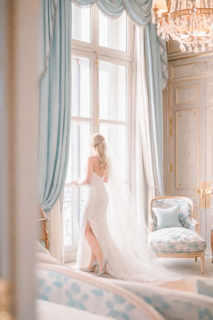 Une mariée dans sa robe Dior qui pose devant la fenêtre de sa suite de luxe au Ritz de Paris